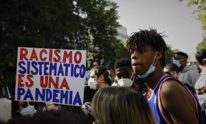 Participante alza un cartel que dice 'Racismo sistemático es una pandemia' en la concentración convocada por la Comunidad Negra, Africana y Afrodescendiente de España frente a la Embajada de EEUU