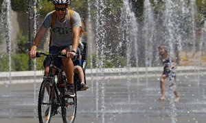 Un padre con su hijo en bicicleta se refrescan en las fuentes del Parque Central de València. - EFE