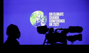 La sombra de una cámara de televisión y un operario junto al logotipo iluminado de la COP26 de Glasgow.