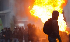 Un hombre camina frente a un contenedor en llamas mientras estallan los enfrentamientos a causa de las medidas restrictivas en Bruselas el 21 de noviembre de 2021.