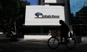 Una mujer en bicicleta pasa por las inmediaciones de la sede de Unicaja Banco en Málaga. E.P./Álex Zea