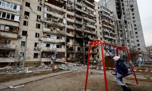 Un niño en un columpio frente a un edificio residencial dañado este viernes por la artillería rusa, en Kiev, Ucrania