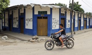 (19/02/2022)  Una persona mientras pasa en moto frente a varios grafitis de las FARC.