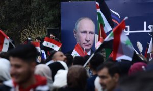 Estudiantes sirios ondean las banderas siria, rusa y palestina debajo de una valla publicitaria con el retrato del presidente ruso Vladimir Putin, en Alepo a 10 de marzo de 2022 .