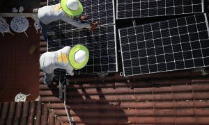 Dos operarios colocan paneles solares en el tejado de una vivienda.