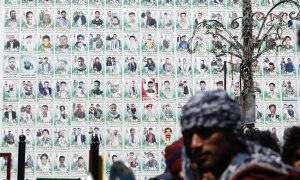 Los yemeníes se paran frente a una enorme pancarta que muestra los retratos de los combatientes hutíes presuntamente asesinados en el conflicto en curso, en una calle antes del séptimo aniversario de la campaña militar dirigida por Arabia Saudita en Yemen