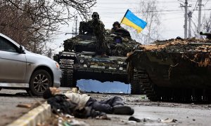 Soldados del ejército ucraniano se sientan en la parte superior de su tanque mientras el cuerpo de un civil yace en la calle en Bucha.