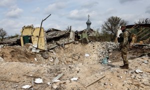 16/04/2022 Un militar ucraniano mira jacia un cráter y una casa destruida en la localidad de Yatskivka, en el este del país