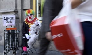 Rayito, un mendigo disfrazado de payaso, saluda sentado junto a un cartel que dice "Quiero comer, gracias" en la calle Gran Vía, en el centro de Madrid, el 28 de octubre de 2014.