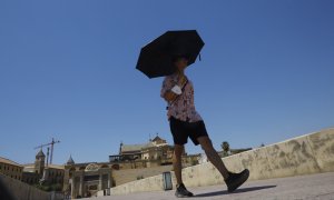 (10/6/2022) Un turista se protege del sol con un paraguas a su paso por el Puente Romano con la Mezquita-Catedral de Córdoba.