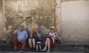 Unos turistas descansan y beben agua sentados a la sombra en los alrededores de la Mezquita-Catedral en Córdoba