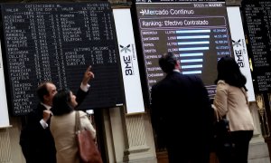 Cuatro personas frente a un panel de valores del Ibex 25 en el Palacio de la Bolsa, a 30 de mayo de 2022, en Madrid.