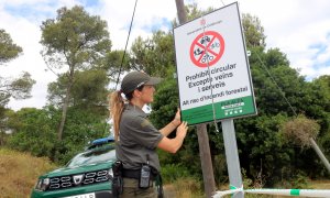 07/07/2022 - Una agent rural col·loca un cartell que informa del tancament del Parc Natural del Montgrí.