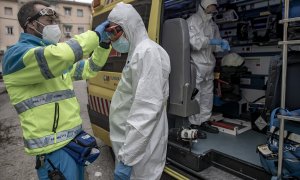 Un trabajador de una UVI móvil del SUMMA 112 se viste con un EPI con la ayuda de otro trabajador durante una jornada de trabajo, en Madrid.