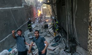 578/22 Dos personas piden ayuda entre los escombros del edificio atacado por el Ejército israelí en Gaza,, mientras un bombero sofoca las llamas