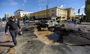 Un oficial de Policía pasa junto a un coche destruido tras un bombardeo en el centro de Kiev.