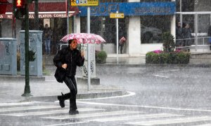 Una mujer pasa esta mañana por una calle de Compostela, enfrentándose a fuertes lluvias y a un intenso viento de una profunda borrasca procedente del Atlántico.