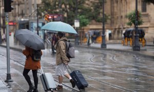 Una pareja con maletas se protegen de la lluvia bajo sus paraguas en Sevilla-21/10/2022