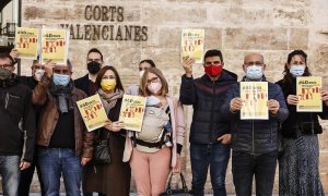 Imagen de archivo en la que varias personas sostienen el 'Informe de Denuncias de los derechos lingüísticos en el País Valencià, frente a las puertas de Les Corts, en diciembre de 2021.