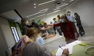 A la izquierda de la imagen, varios miembros de una mesa electoral atienden a los votantes en los comicios del 4 de mayo de 2021 en Madrid