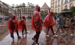 Un grupo de personas se tapan de la lluvia y el viento en una calle de Málaga, a 18 de mayo de 2023.