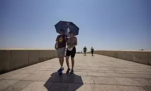 Una pareja de turistas caminan bajo un paraguas para paliar los rayos de sol por el Puente Romano de Córdoba, donde los termómetros rondan los 44ºC.