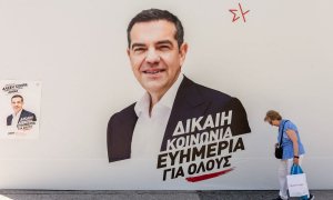 Una mujer pasa por delante de un puesto de campaña de Syriza con una foto del líder del partido Alexis Tsipras en el centro, a 25 de junio de 2023, en Atenas.