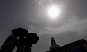 Varios viandantes se protegen del sol mientras cruzan la Puerta del Sol de Madrid.