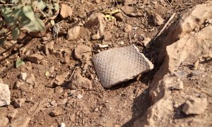 Un tros d'amiant enmig de la sorra i les pedres a la zona de les bateries del Turó de la Rovira