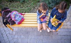 Niñas de la escuela sentadas en un banco en el patio de la escuela y comiendo de las loncheras