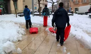 Trens nens amb trineus creuen la plaça plena de neu a Horta de Sant Joan, durant el temporal del febrer del 2023