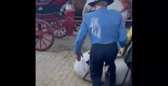 Dos hombres patean a un caballo agotado que se desplomó durante la Feria de Abril de Sevilla