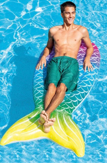 Un hombre disfruta de la piscina recostado en una colchoneta en forma de cola de sirena.,