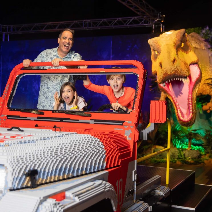 Una familia posa en un Jeep fingiendo su huida de un tiranosaurio rex construido con piezas Lego. Foto: Anna Kucera, cedida por Proactiv Entertainment